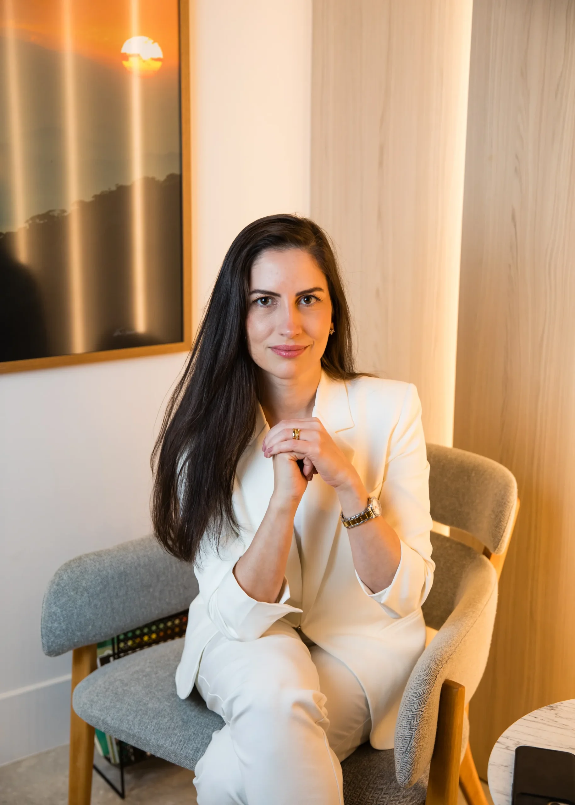 Dra. Renata Pina Barata sentada, de blazer claro, em seu consultório